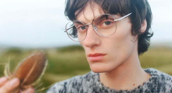 Close-up portrait of a person wearing metal eyeglass frames outdoors.