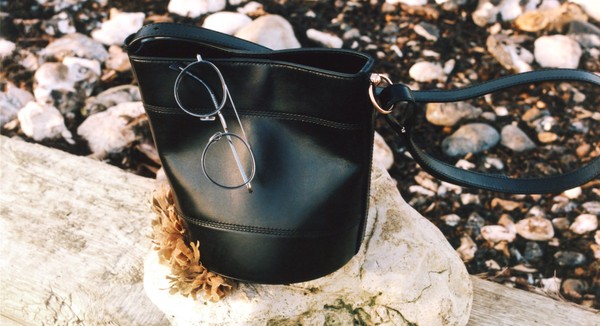 Still life of thin metal glasses hooked onto a handbag outdoors.