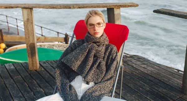 Person lounging on a red deckchair by the sea, wearing narrow rectangular glasses.