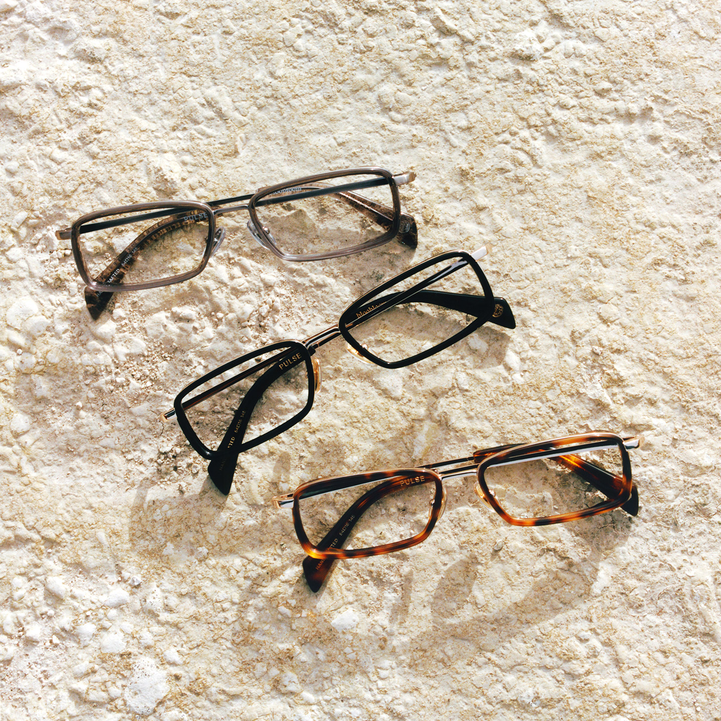 Three pairs of rectangular eyeglass frames arranged on a textured stone surface.