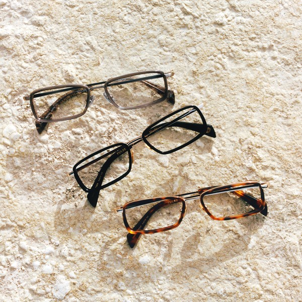 Three pairs of rectangular eyeglass frames arranged on a textured stone surface.