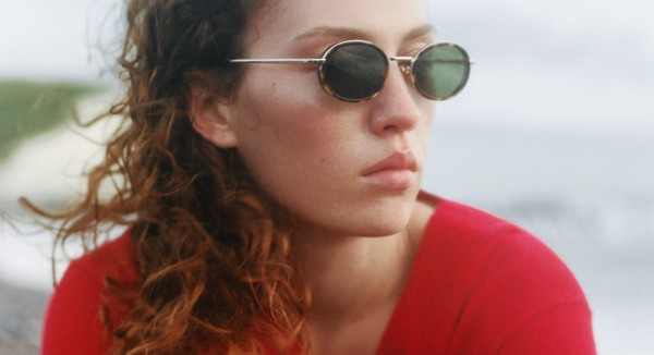 Lifestyle close-up of sunglasses with gold temples on a beach setting.