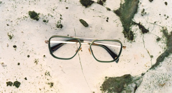 Optical frames in green acetate with gold bridge on a speckled rock surface.