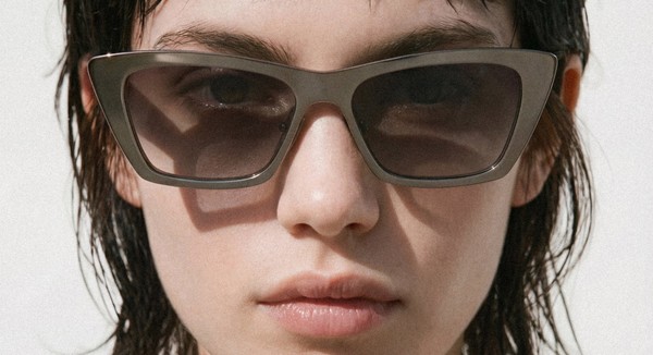 Person wearing dark, rectangular sunglasses with angled corners, photographed straight-on against a light background.