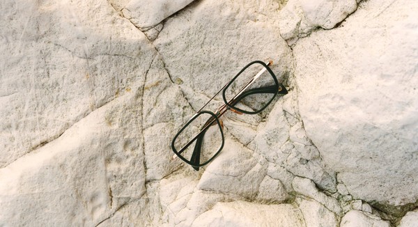 Green-and-gold optical frames placed on a textured stone surface.