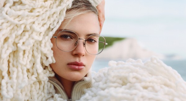 Tight face shot highlighting round glasses and textured knit layers.