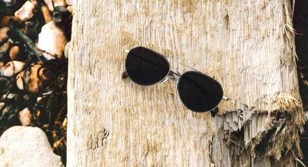 Black-lens sunglasses on driftwood, warm coastal still life.