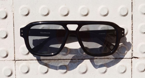 Black bloobloom sunglasses photographed on white textured paving.