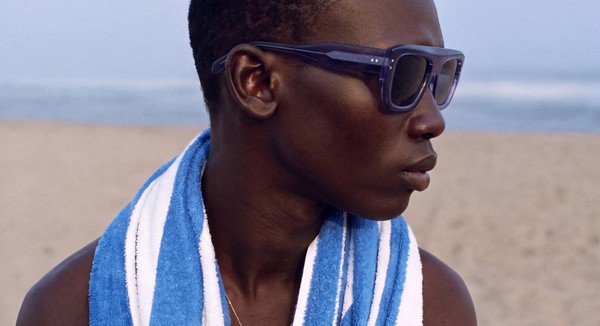 Model in blue sunglasses with a striped towel on a beach