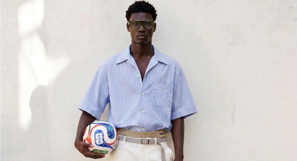 Model in green glasses holding a football against a white wall