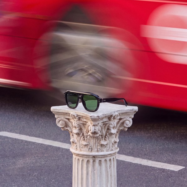 Black bloobloom sunglasses on a stone plinth as a red London bus passes behind.