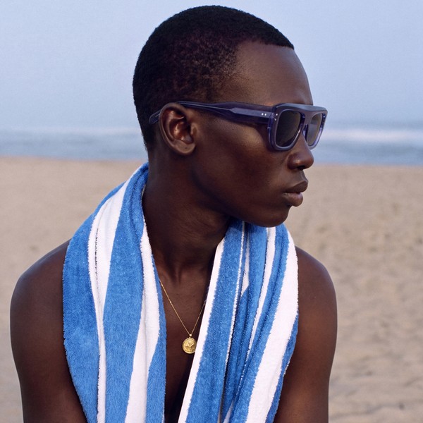 Model in blue sunglasses with a striped towel on a beach