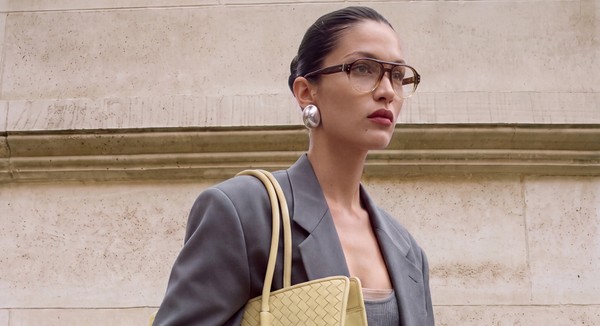 Model wearing brown glasses and grey tailoring with a woven yellow handbag.
