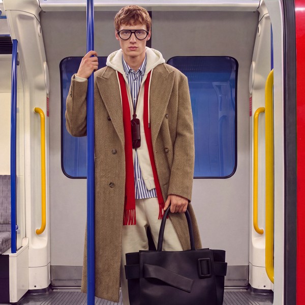 Model wearing blue glasses and layered tailoring inside a London Underground train.