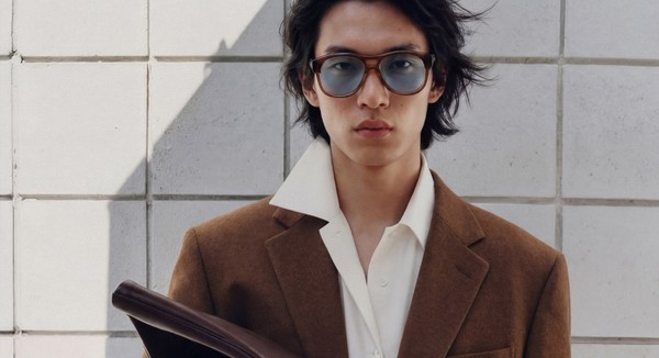 Fashion model wearing brown acetate eyeglasses and tailored blazer against minimalist tiled wall background