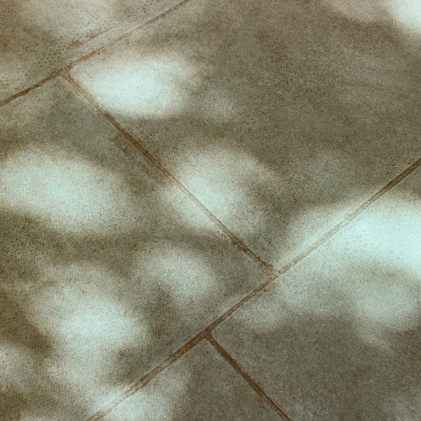 Abstract shadows cast across textured stone paving in sunlight.