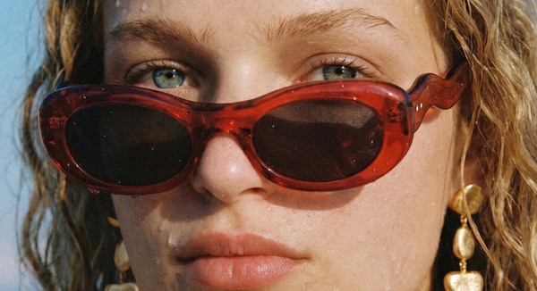 Close-up portrait of a female model wearing red FLOW sunglasses with water droplets on the skin.