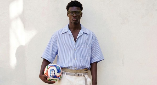 Model in green glasses holding a football against a white wall