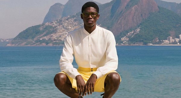 Male model wearing FLOW optical glasses by the waterfront in Rio de Janeiro, dressed in a cream shirt and yellow shorts.